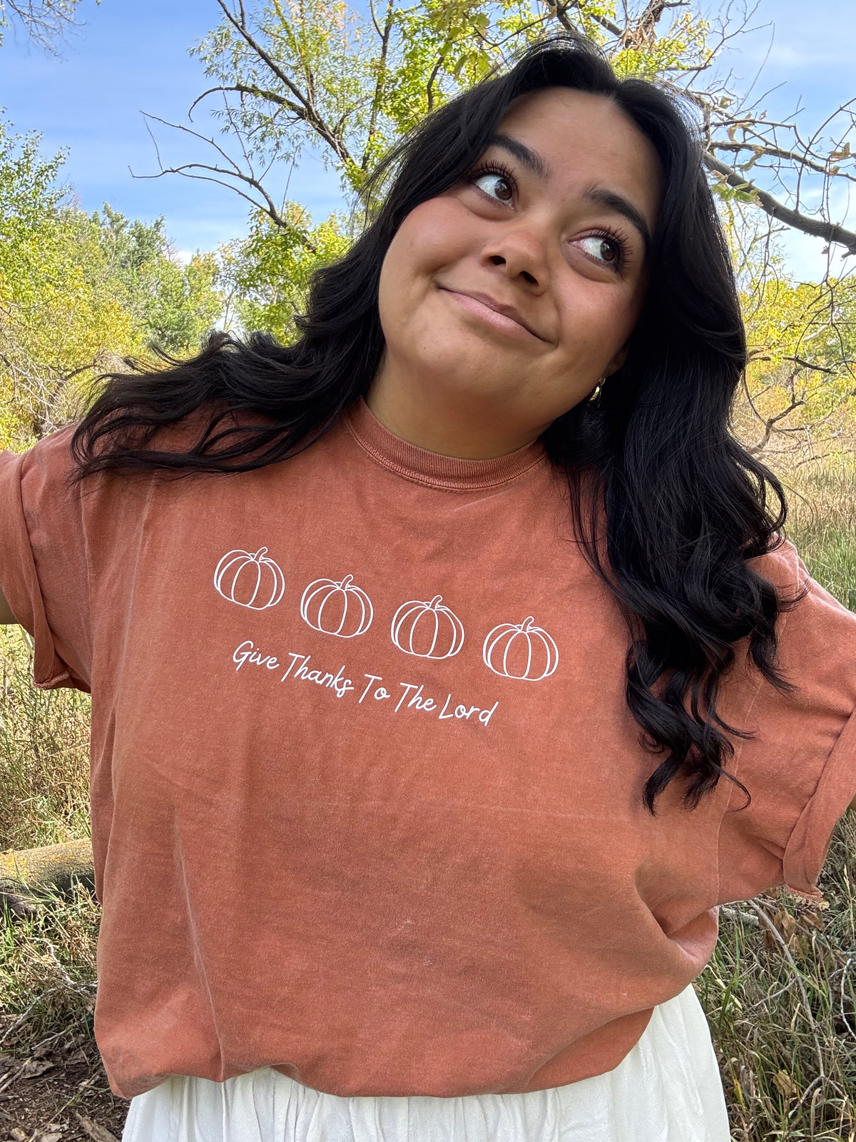 Person wearing an orange comfort colors tshirt with pumpkin design and text outdoors